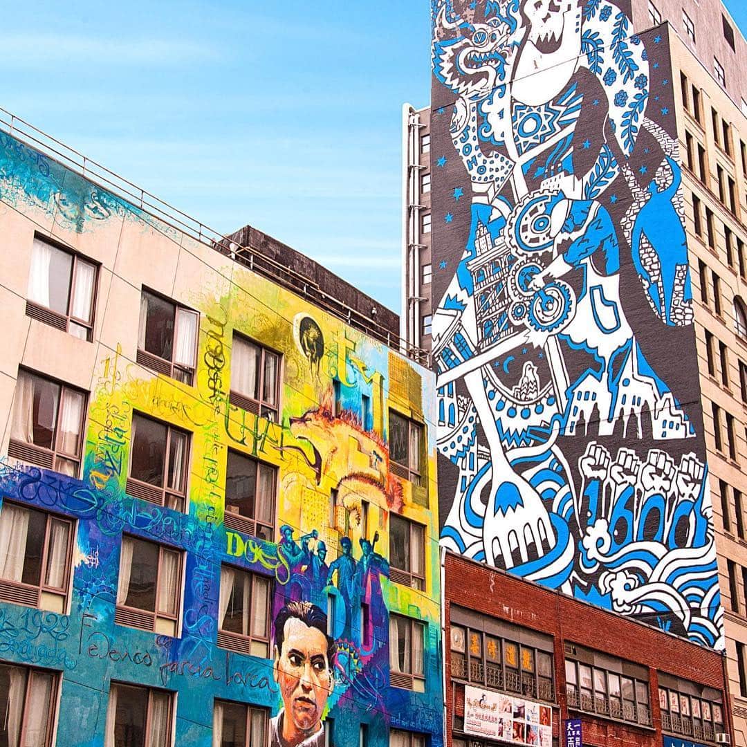 Edificios cubiertos de murales en azul y blanco, con un retrato pintado en la planta baja, bajo un cielo despejado.