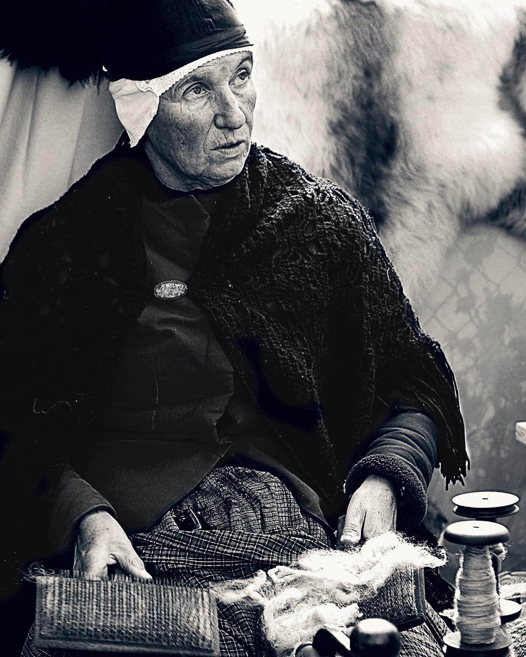 Retrato en blanco y negro de una mujer mayor con pañuelo en la cabeza, hilando con las manos.