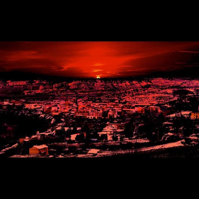 Vista de una ciudad al amanecer bajo un cielo de nubes, con toda la escena virada a rojo intenso.