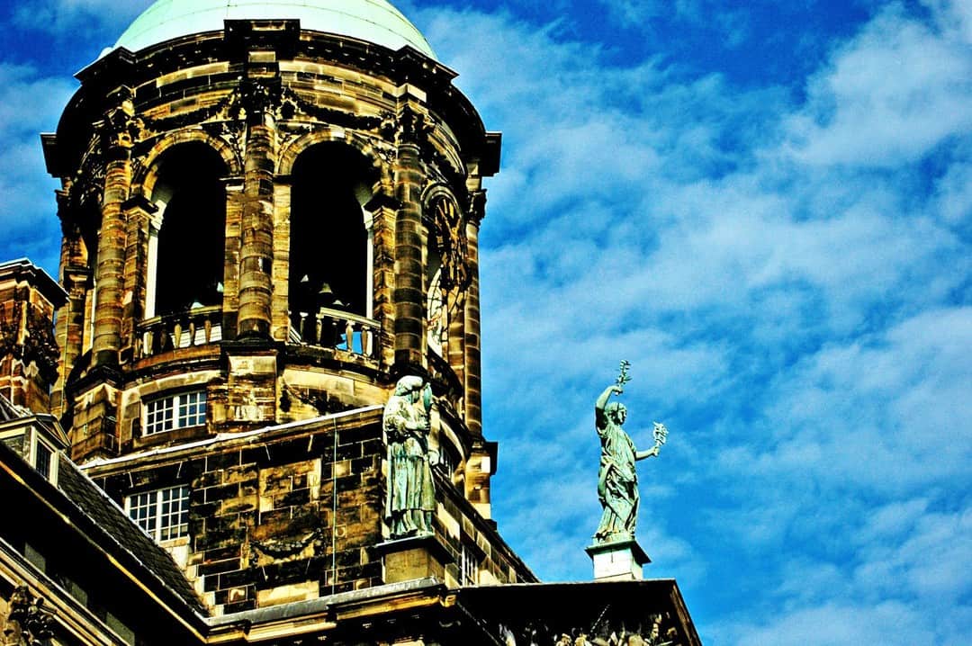 Torre del campanario de Ámsterdam con una figura dorada, recortada contra un cielo azul con nubes.
