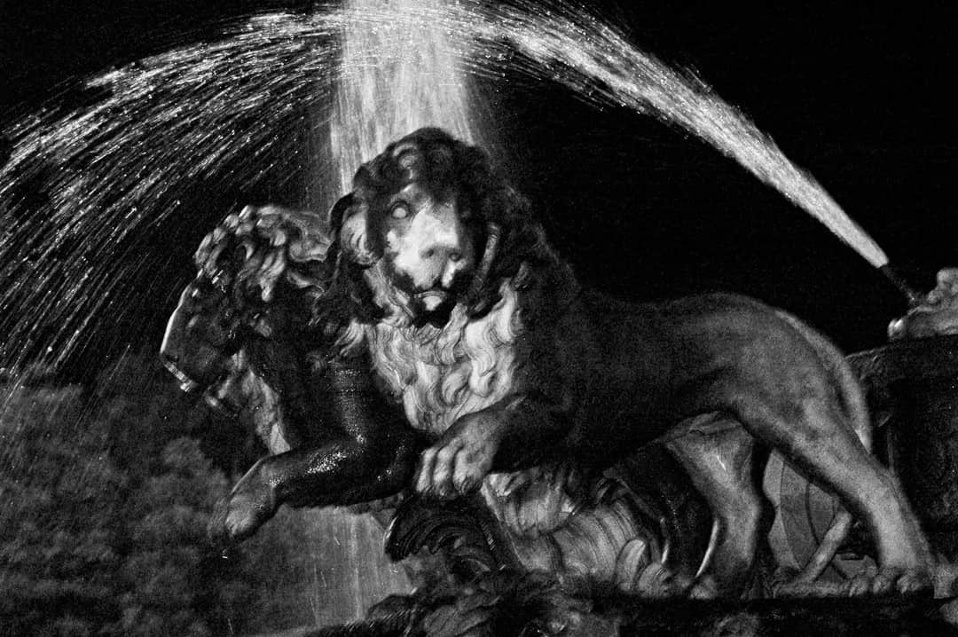 Grupo escultórico de una fuente con figuras y un chorro de agua, en blanco y negro de alto contraste.