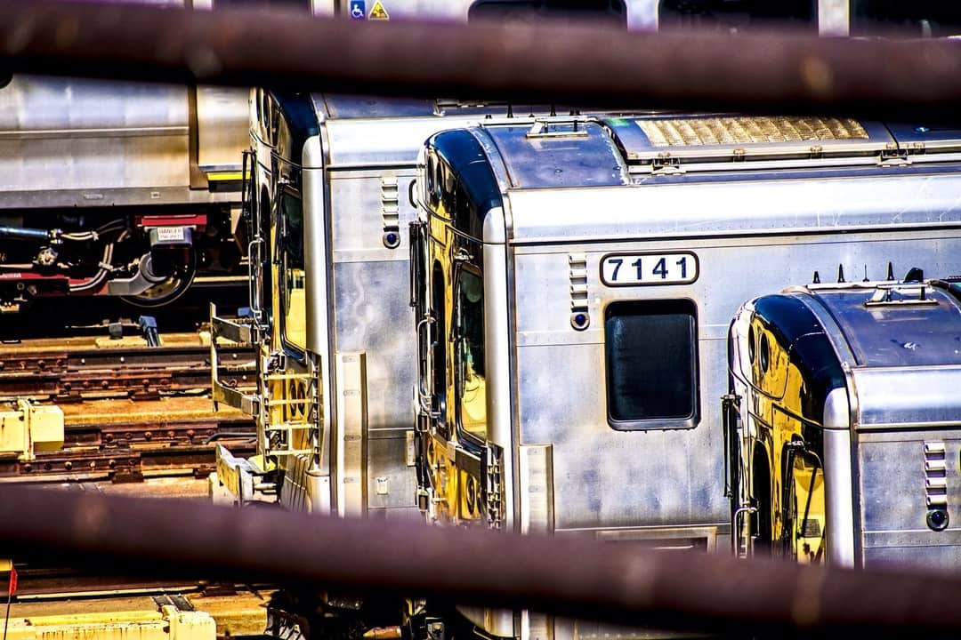 Trenes plateados aparcados, vistos a través de los barrotes de una valla.