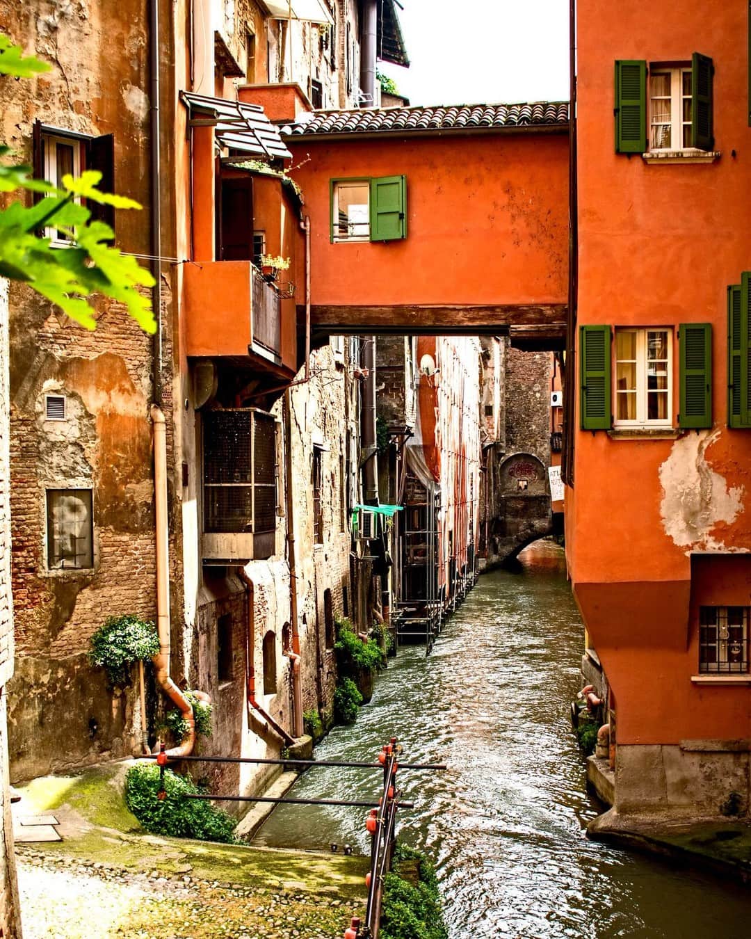 Canal estrecho entre casas de fachadas anaranjadas con ventanas de postigos verdes.