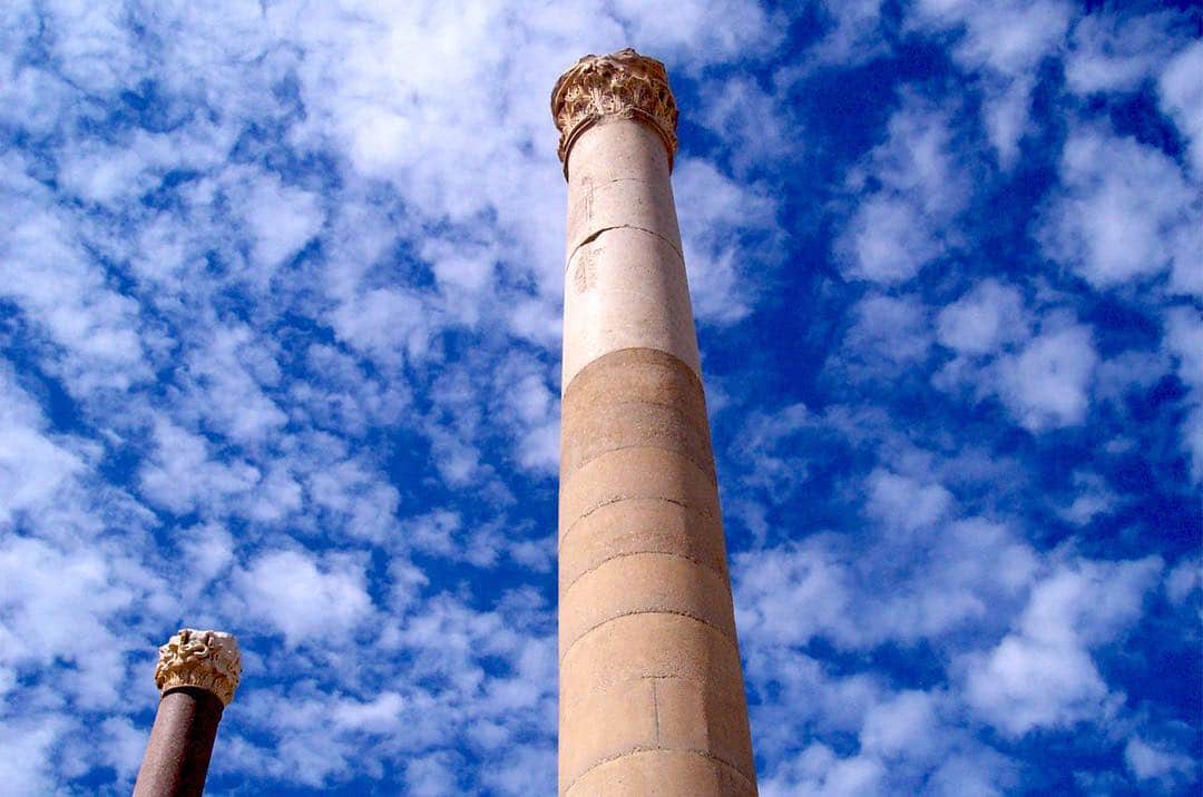 Columna de piedra vista desde abajo contra un cielo azul con nubes blancas.