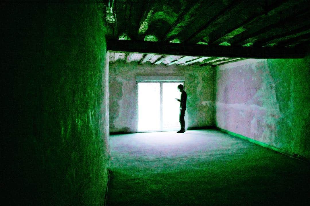 Silueta de una persona asomada a una ventana en una sala vacía, con la imagen virada a verde.