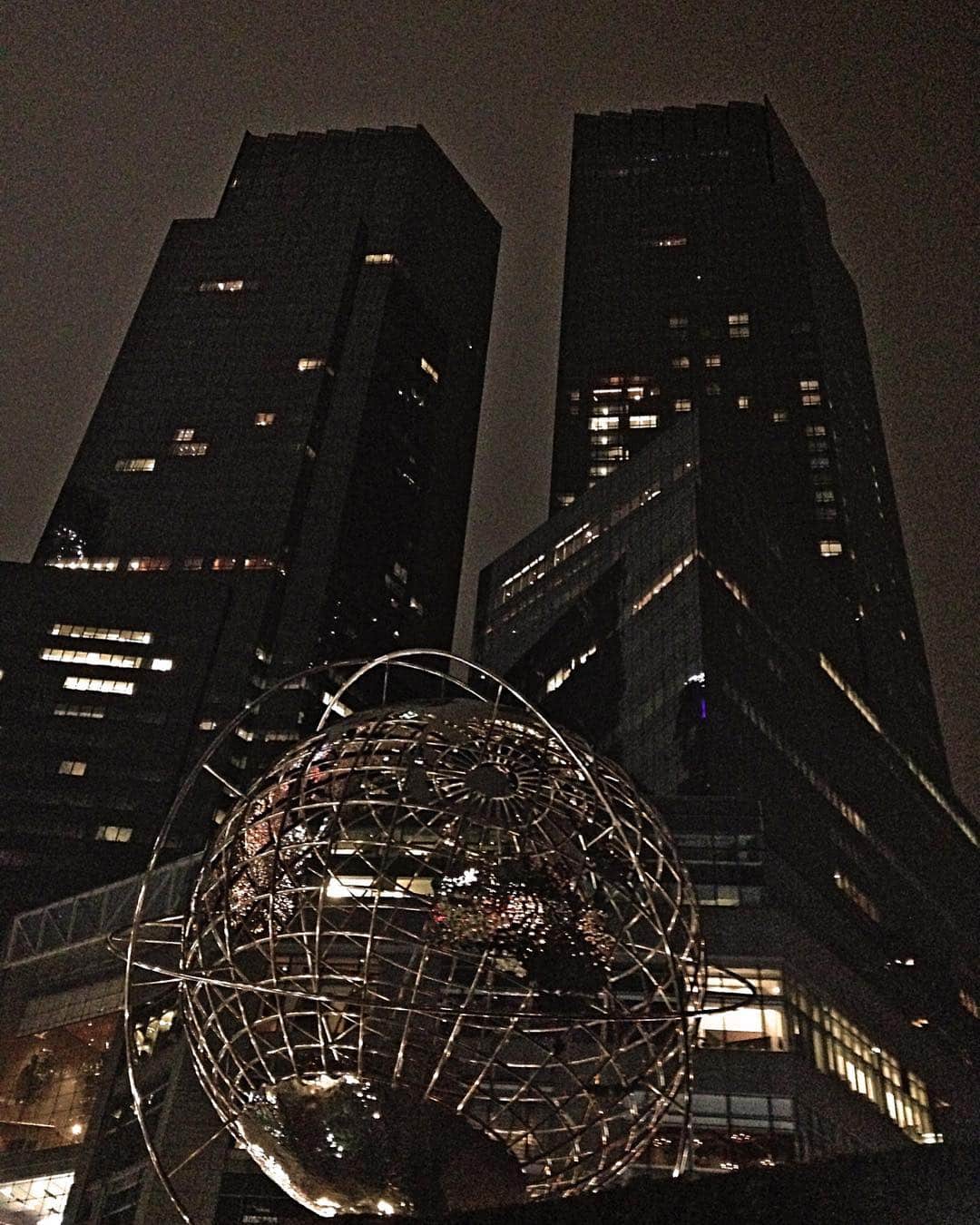 Globo terráqueo de estructura metálica iluminado de noche en Columbus Circle, entre dos torres oscuras de Nueva York.