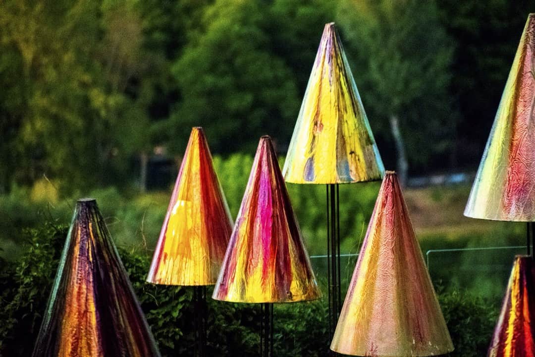 Conos metálicos de colores irisados clavados en el césped de un jardín.
