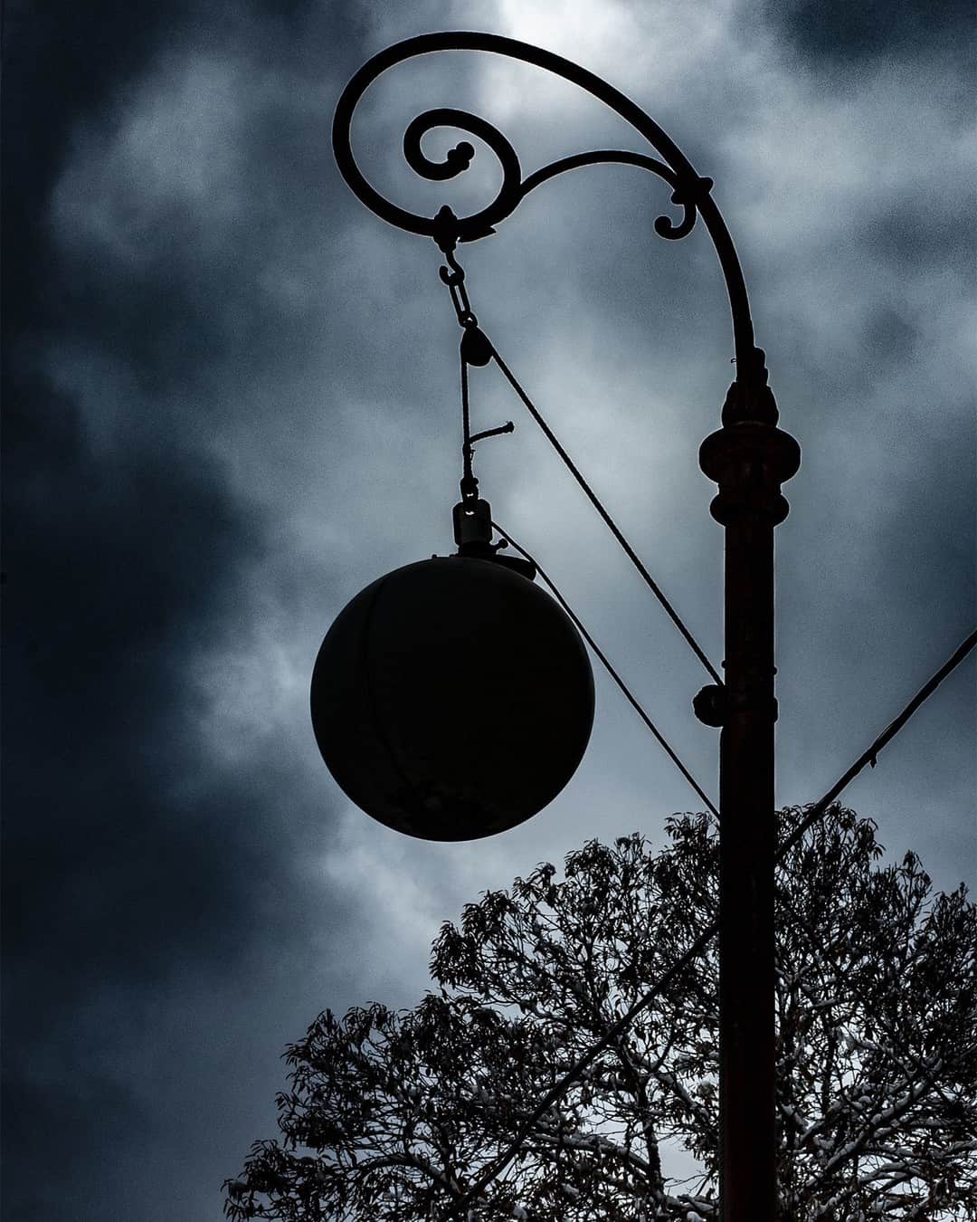 Farola antigua con un globo de cristal, recortada contra un cielo de nubes oscuras, casi monocroma.