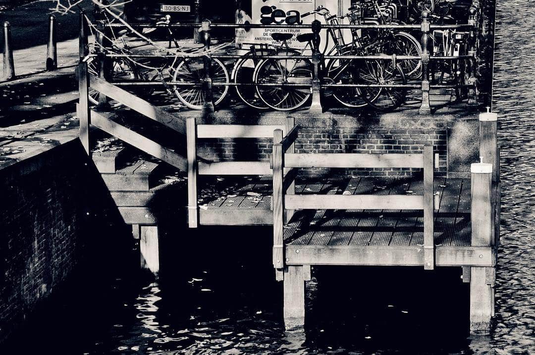Embarcadero de madera sobre el agua, con bicicletas aparcadas encima, en blanco y negro de alto contraste.
