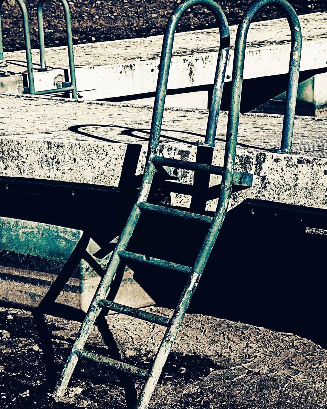 Escalera metálica de una piscina vacía, apoyada sobre el hormigón agrietado y sin agua.