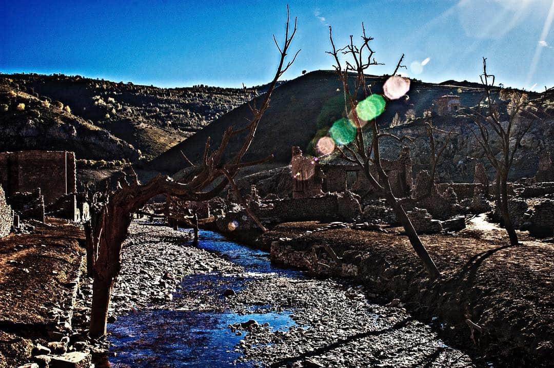 Cauce seco y pedregoso al pie de una ladera, con árboles desnudos y un charco de agua.