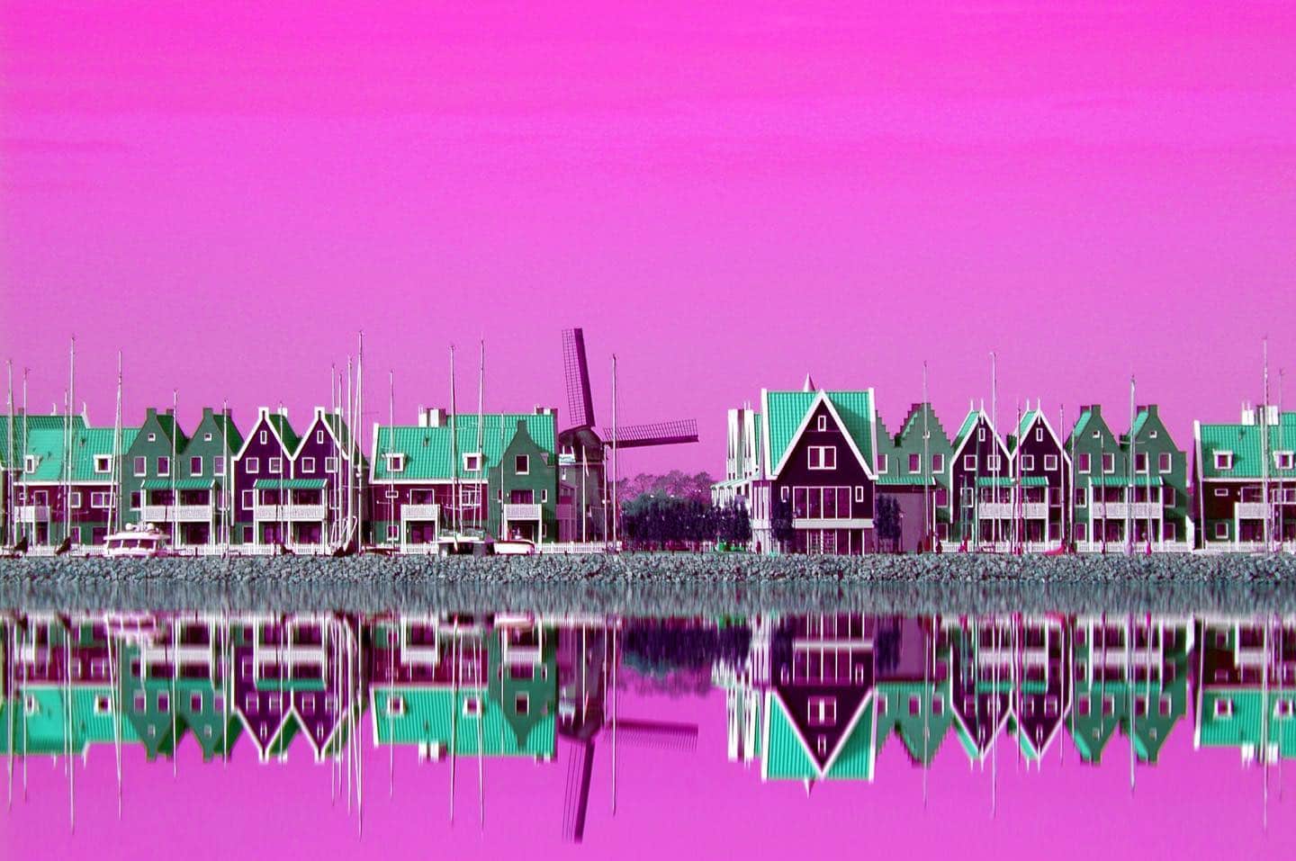 Casas de un pueblo holandés reflejadas en el agua, con la imagen virada a rosa y turquesa.