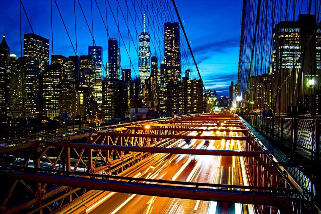 Puente de Nueva York de noche con las estelas de los faros y el perfil de los rascacielos al fondo.