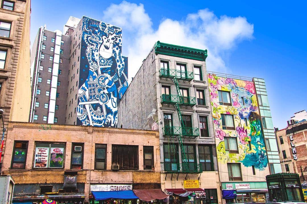 Fachadas de un barrio de Nueva York cubiertas de murales de colores, bajo un cielo azul con nubes.