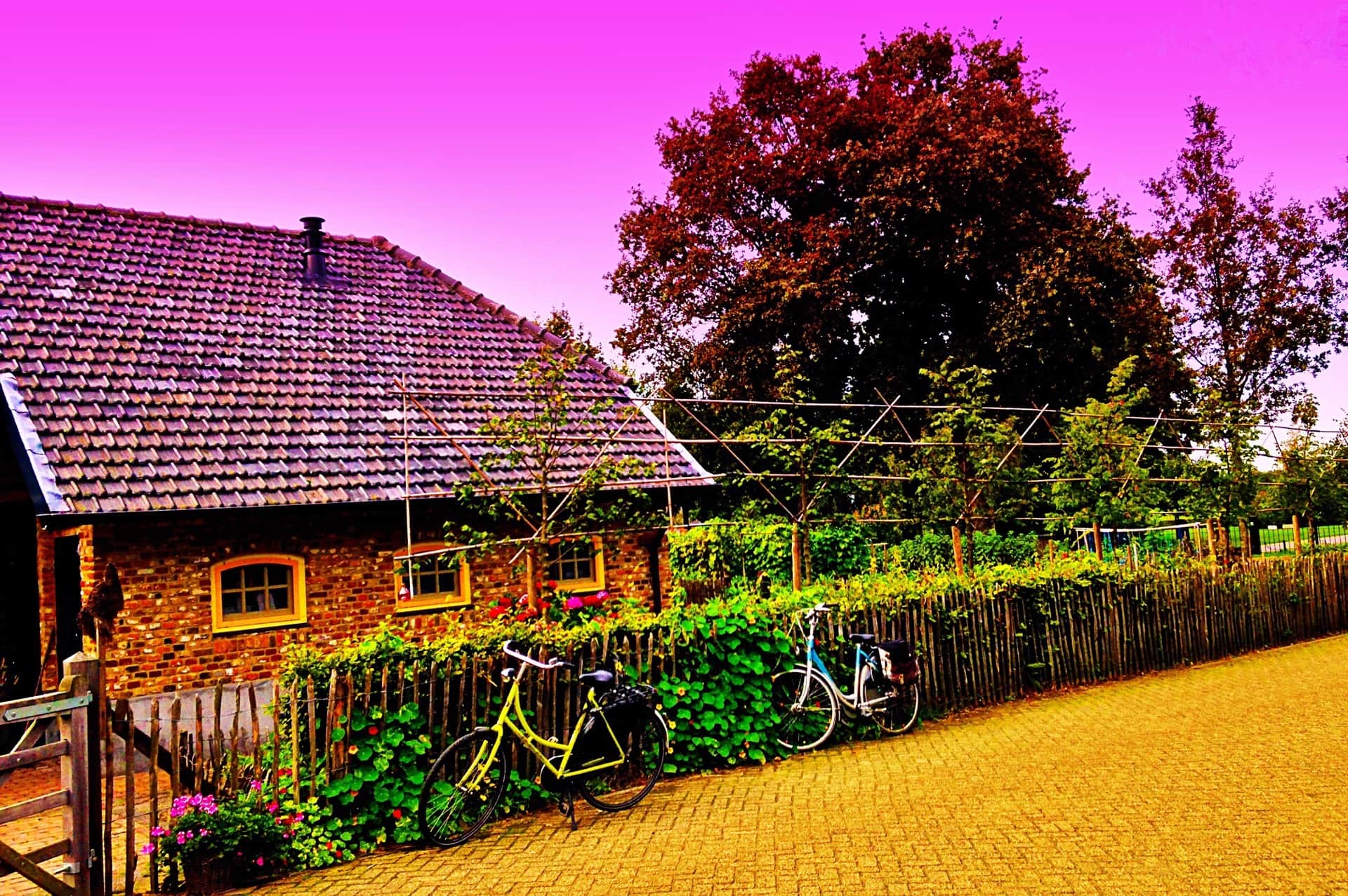 Casa de ladrillo con tejado de teja y dos bicicletas apoyadas en la valla de madera, bajo un cielo magenta.