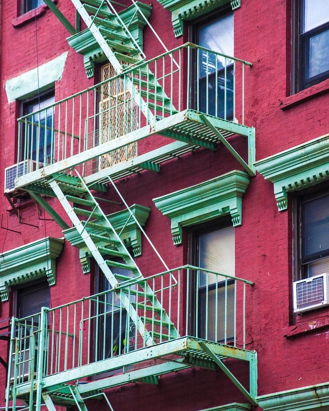 Fachada de ladrillo rojo de un edificio de Nueva York, cubierta por escaleras de incendios pintadas de verde agua.