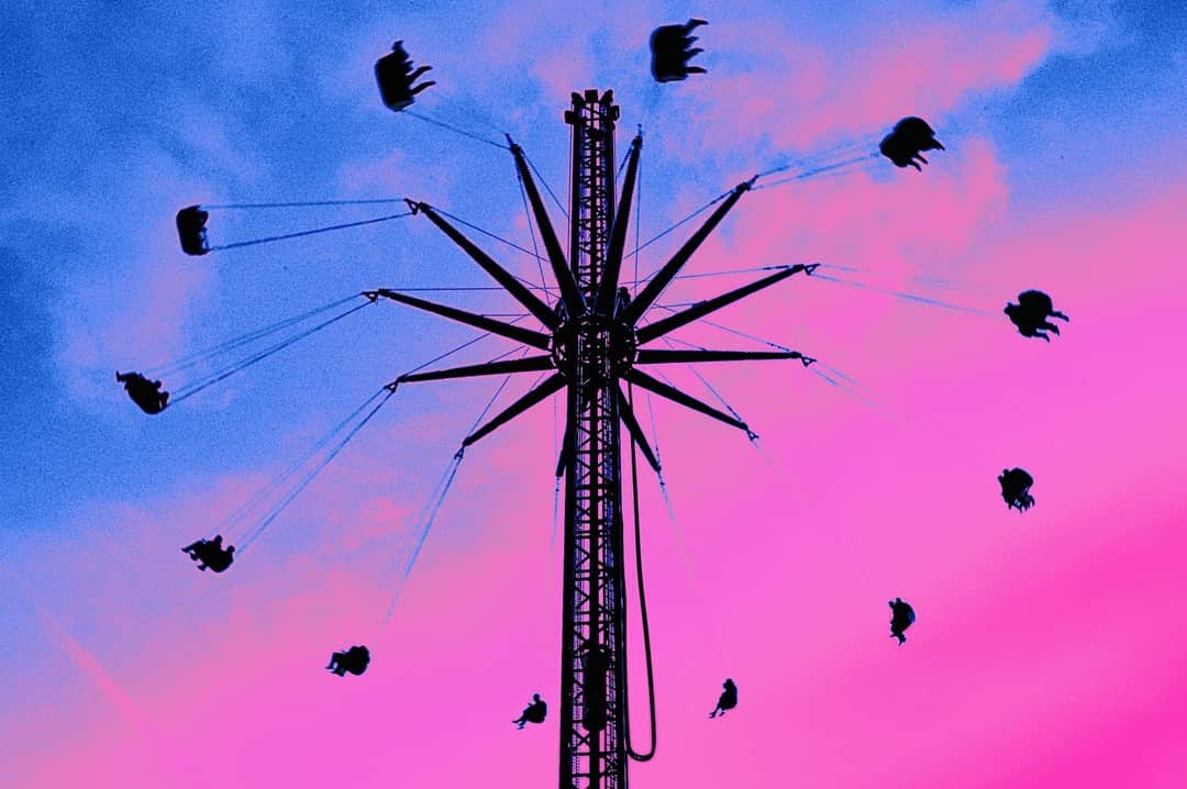Atracción de sillas voladoras girando en lo alto, recortada contra un cielo virado a rosa y azul.
