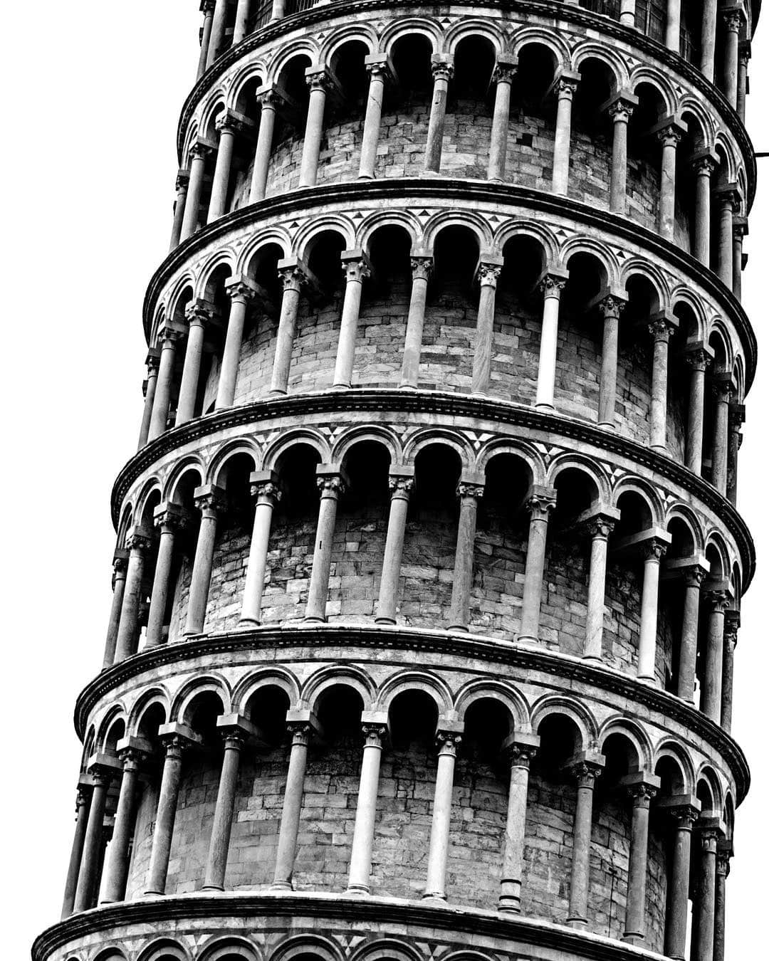 Torre inclinada de Pisa vista desde abajo, con sus galerías de columnas, en blanco y negro.