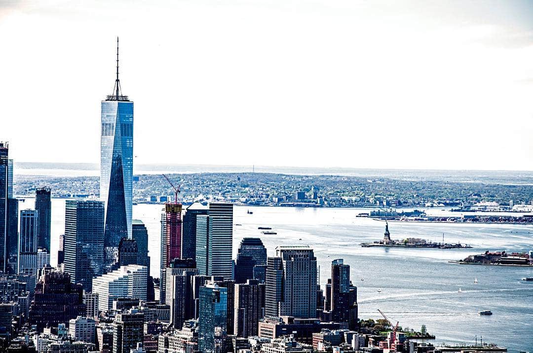 Vista del bajo Manhattan desde el agua, con la torre principal destacando sobre un cielo blanco.