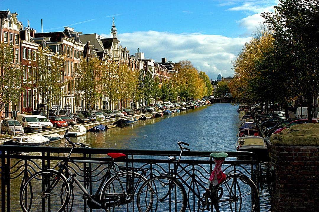 Canal de Ámsterdam con bicicletas apoyadas en la barandilla y las casas alineadas en la orilla.