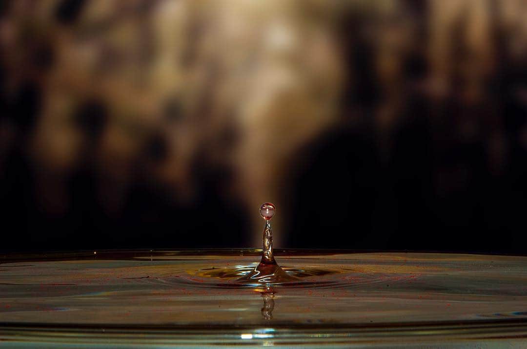 Gota de agua cayendo sobre una superficie líquida y levantando una pequeña columna, con el fondo cálido muy desenfocado.