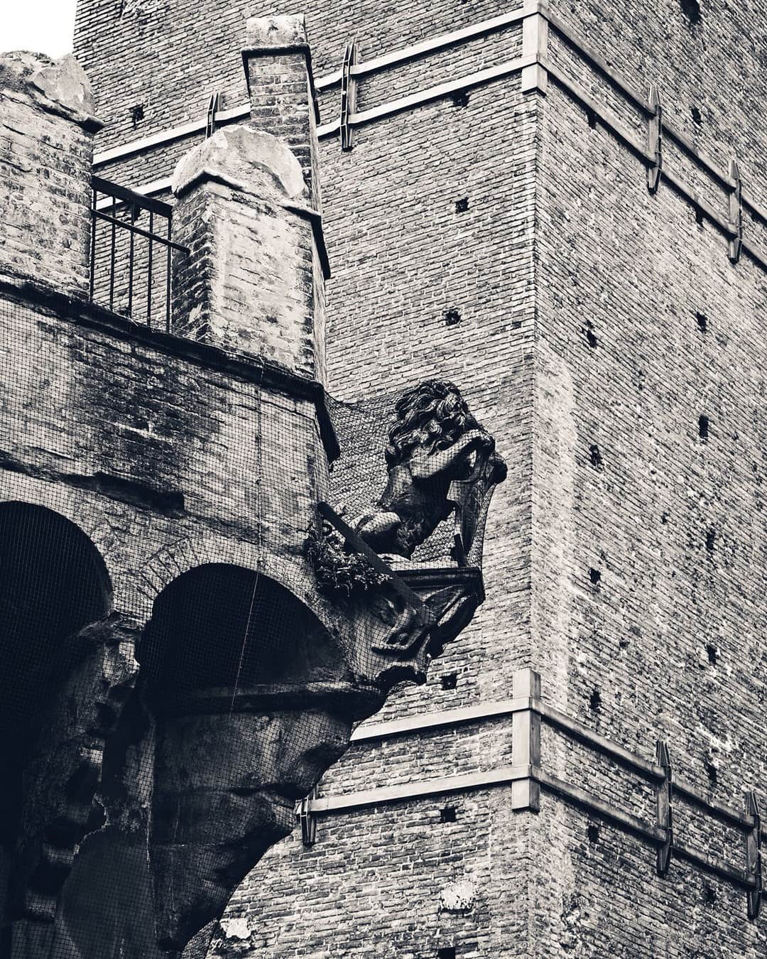 Gárgola con forma de león en la esquina de un edificio de ladrillo, en blanco y negro.