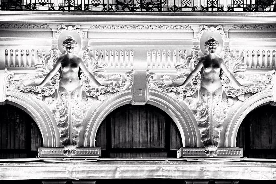 Detalle de una fachada modernista blanca con dos figuras femeninas esculpidas sobre los arcos.