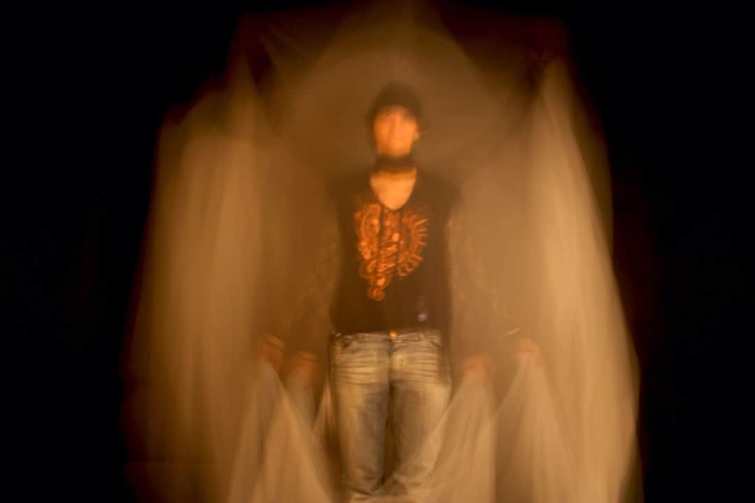 Figura humana desdibujada por una larga exposición, con estelas naranjas sobre fondo oscuro.