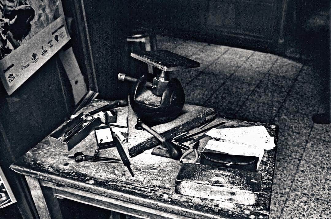 Banco de trabajo de un orfebre con herramientas y un microscopio, en penumbra y casi monocromo.