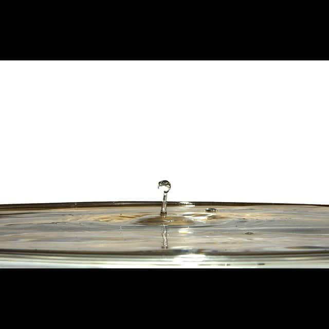 Gota de agua rebotando sobre una superficie líquida y formando una columna, recortada sobre fondo blanco.