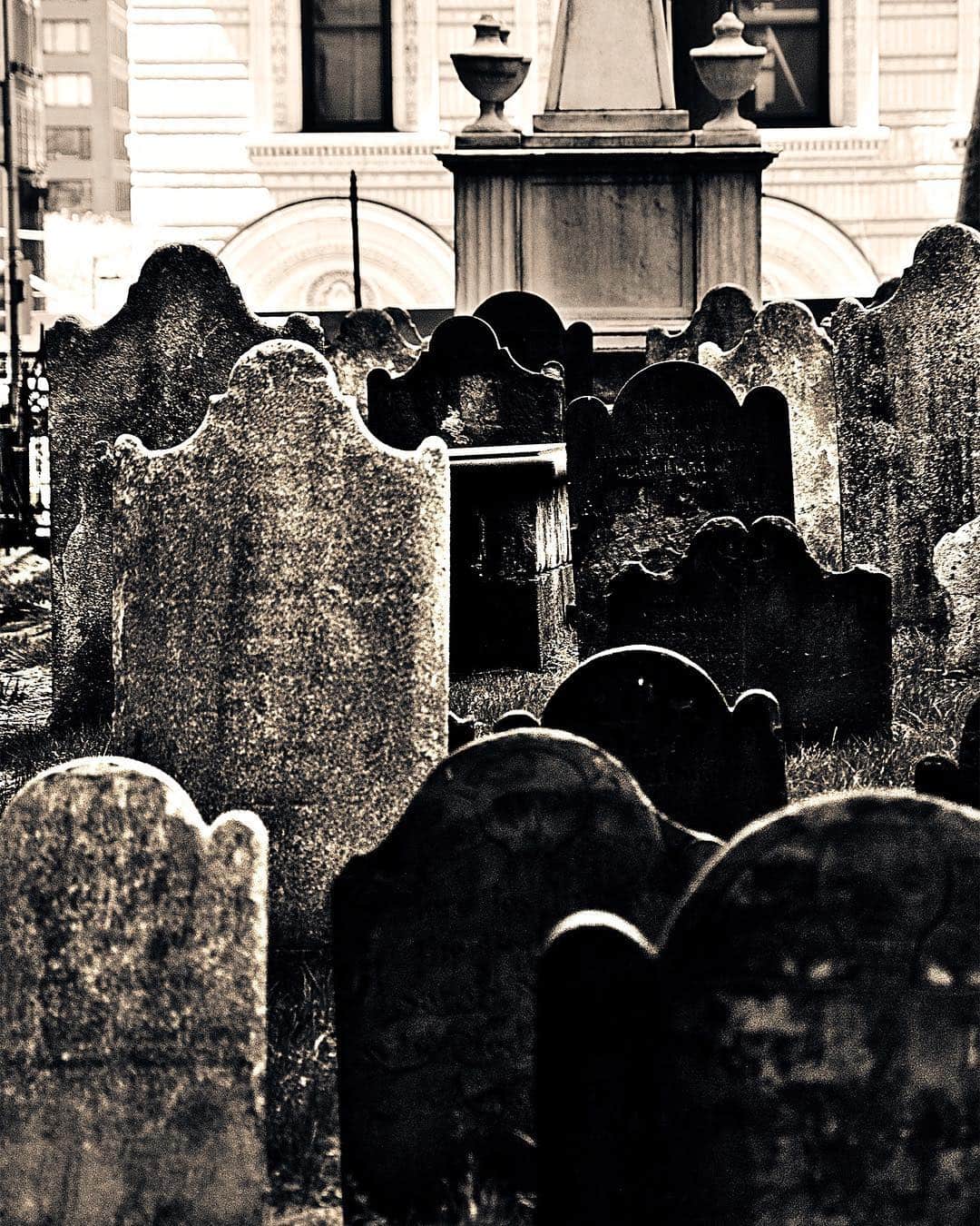 Lápidas antiguas apiñadas en un cementerio junto a un edificio de piedra, en tonos apagados.
