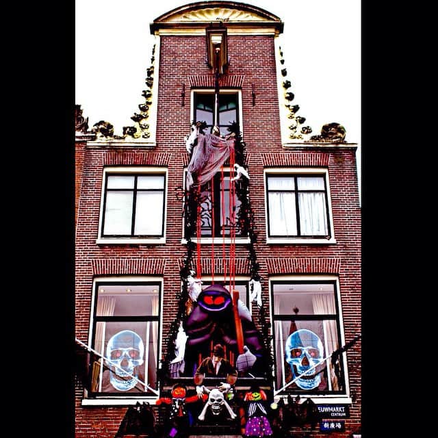 Fachada de una casa de Ámsterdam decorada para Halloween, con una figura colgada del gablete, telarañas y calaveras pintadas en las ventanas.