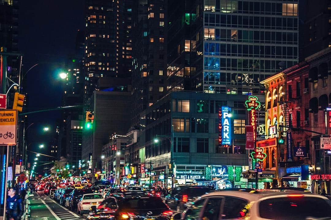 Avenida de Nueva York de noche, con los faros de los coches, los rótulos de neón y los edificios iluminados.