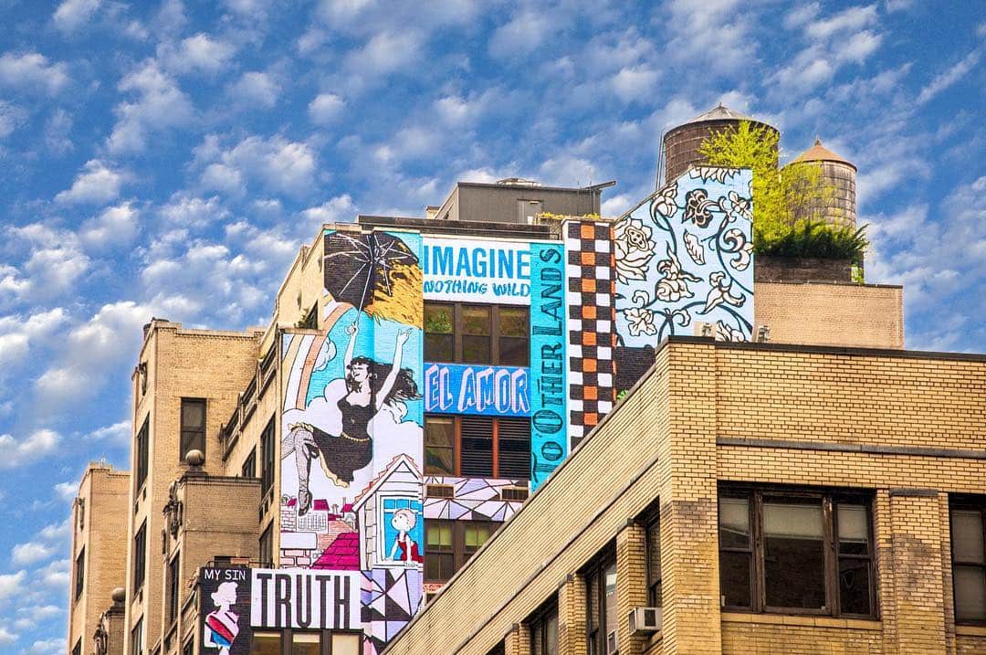 Azotea de un edificio cubierta de murales y carteles de colores, con la palabra «Imagine» visible, bajo un cielo azul con nubes.
