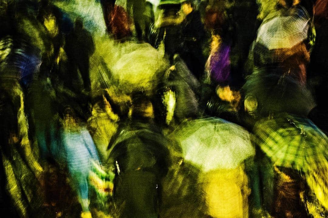 Figuras humanas convertidas en manchas verdes y amarillas por un barrido de cámara, casi abstracto.