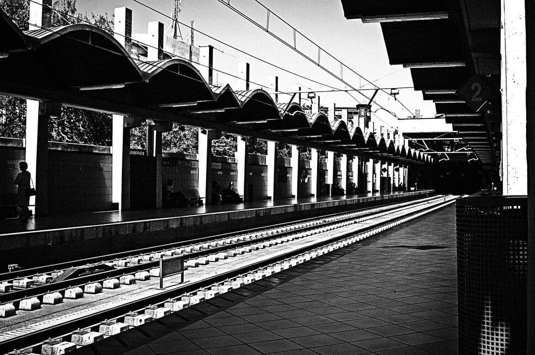 Andén de una estación de tren vacía, con la bóveda de hierro y las vías perdiéndose al fondo, en blanco y negro.