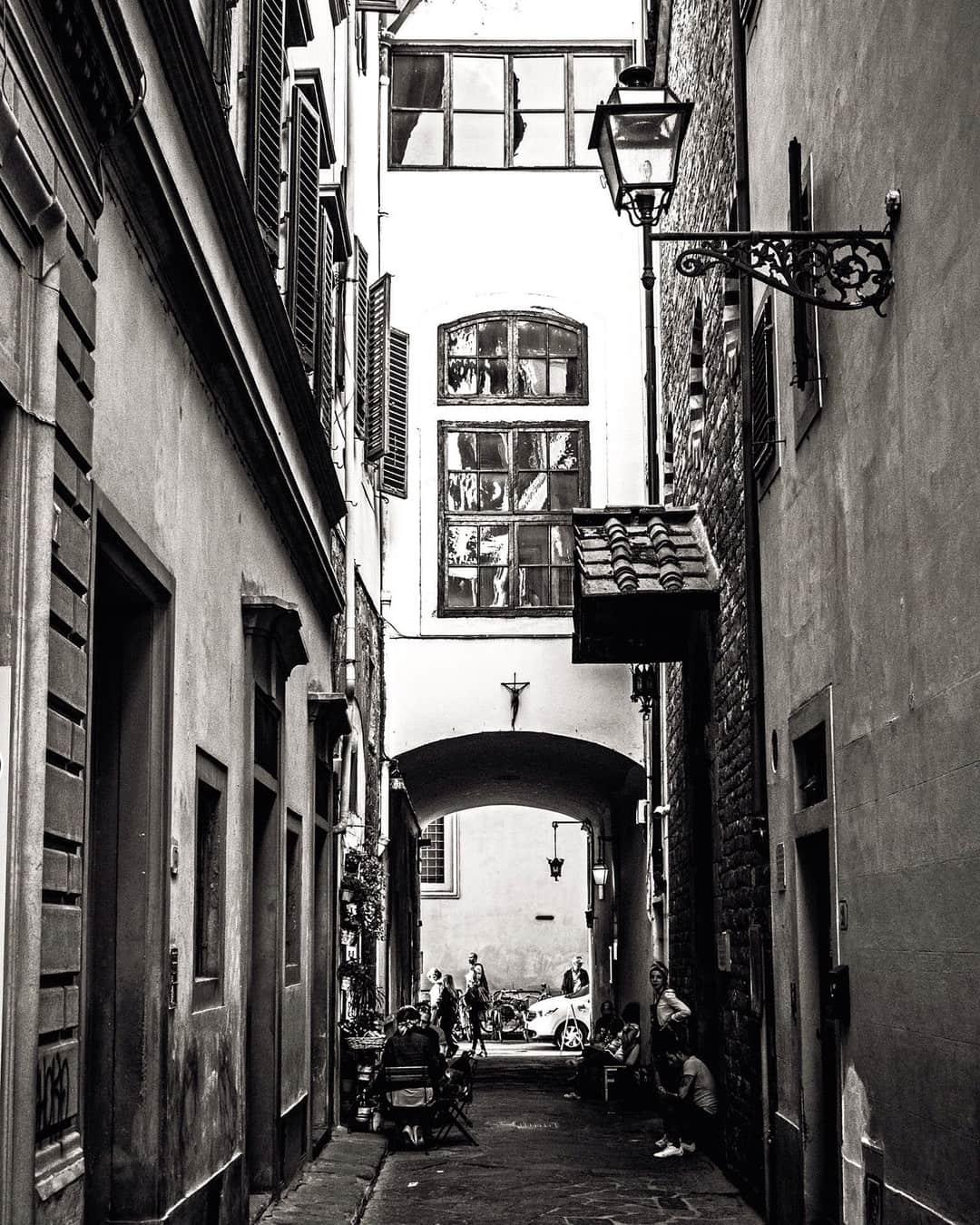 Callejón italiano estrecho entre edificios altos, con un arco al fondo, en blanco y negro.