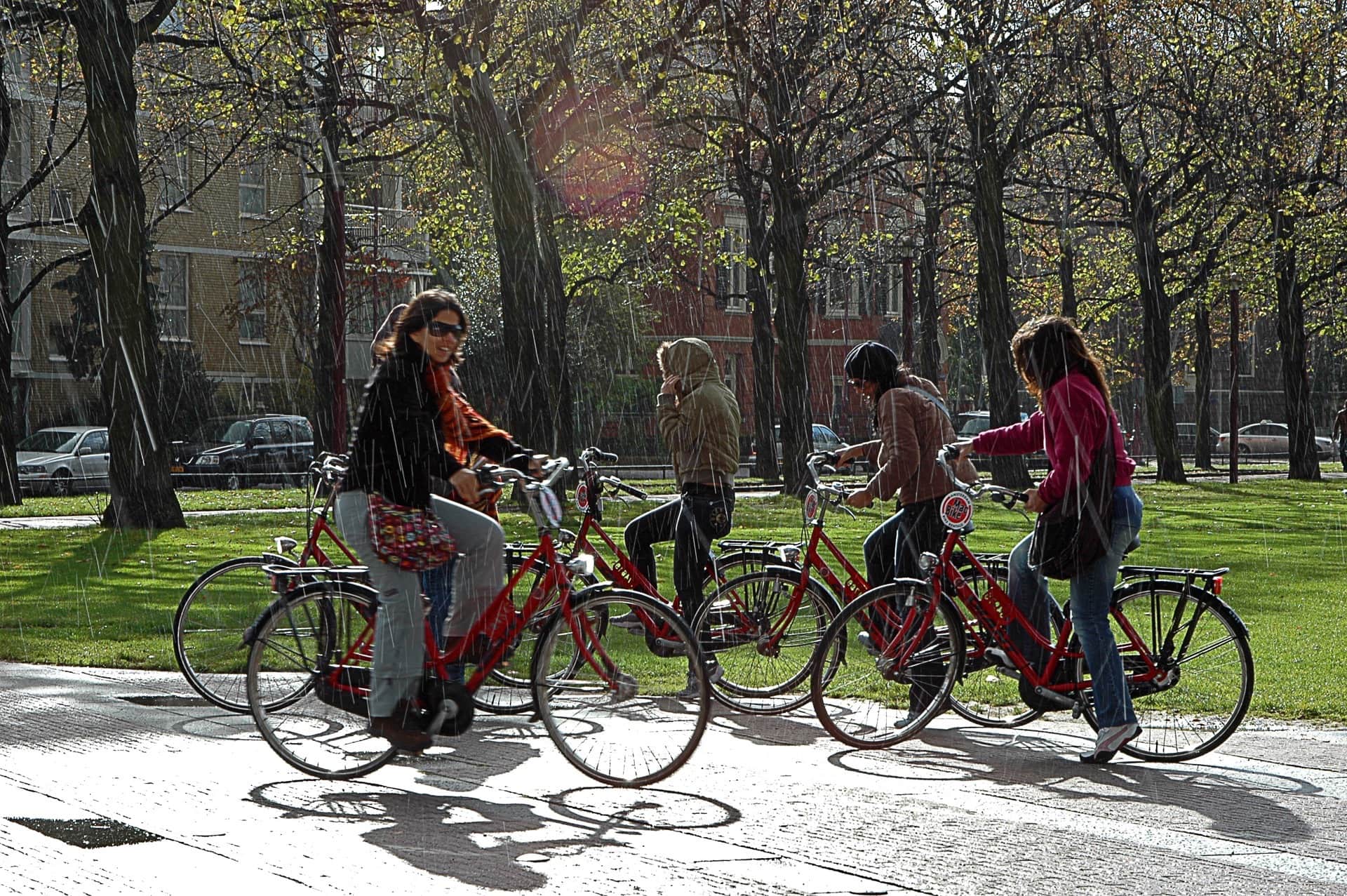 Cuatro jóvenes con bicicletas rojas bajo un chaparrón iluminado a contraluz, en un parque de árboles otoñales