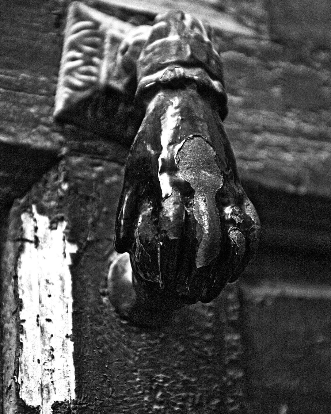 Aldaba de hierro en forma de mano sobre una puerta de madera, en blanco y negro y a contraluz.