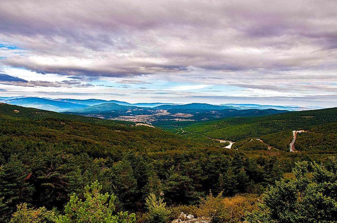Vista de un valle boscoso desde lo alto, con el horizonte lejano bajo un cielo de nubes.