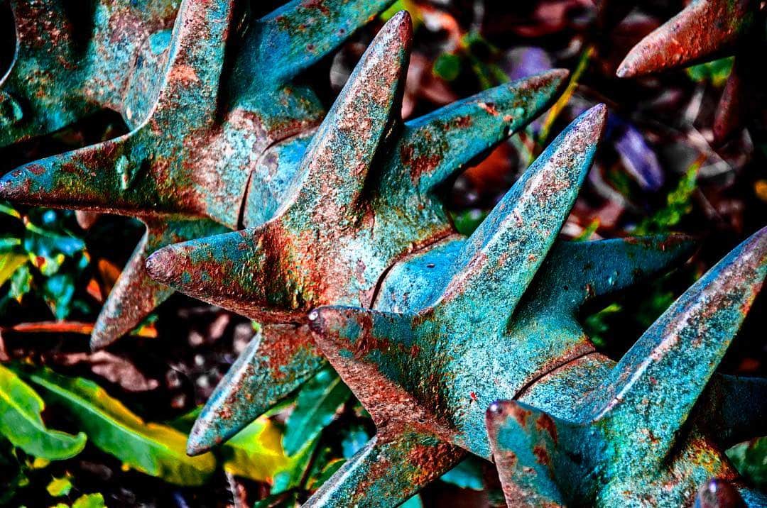 Remates metálicos puntiagudos y oxidados de una verja, vistos de cerca y con los colores muy saturados.