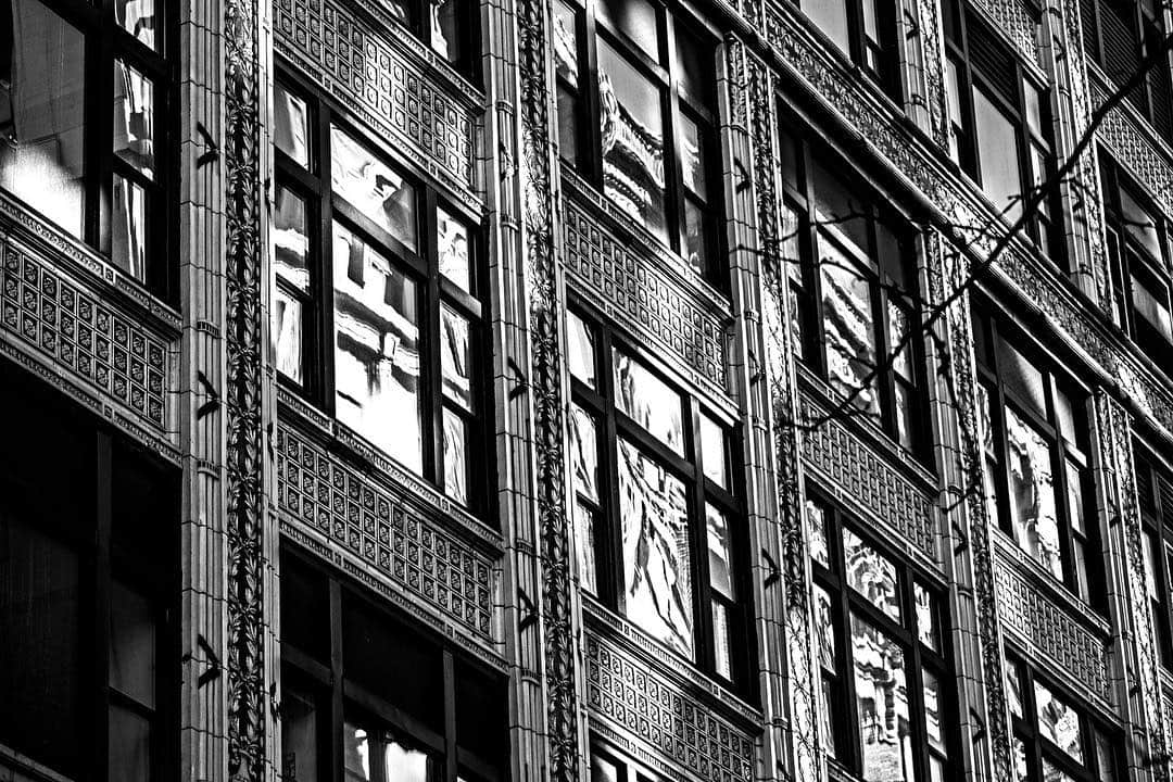 Fachada de un edificio con hileras de ventanas y escaleras de incendios, en diagonal y en blanco y negro.
