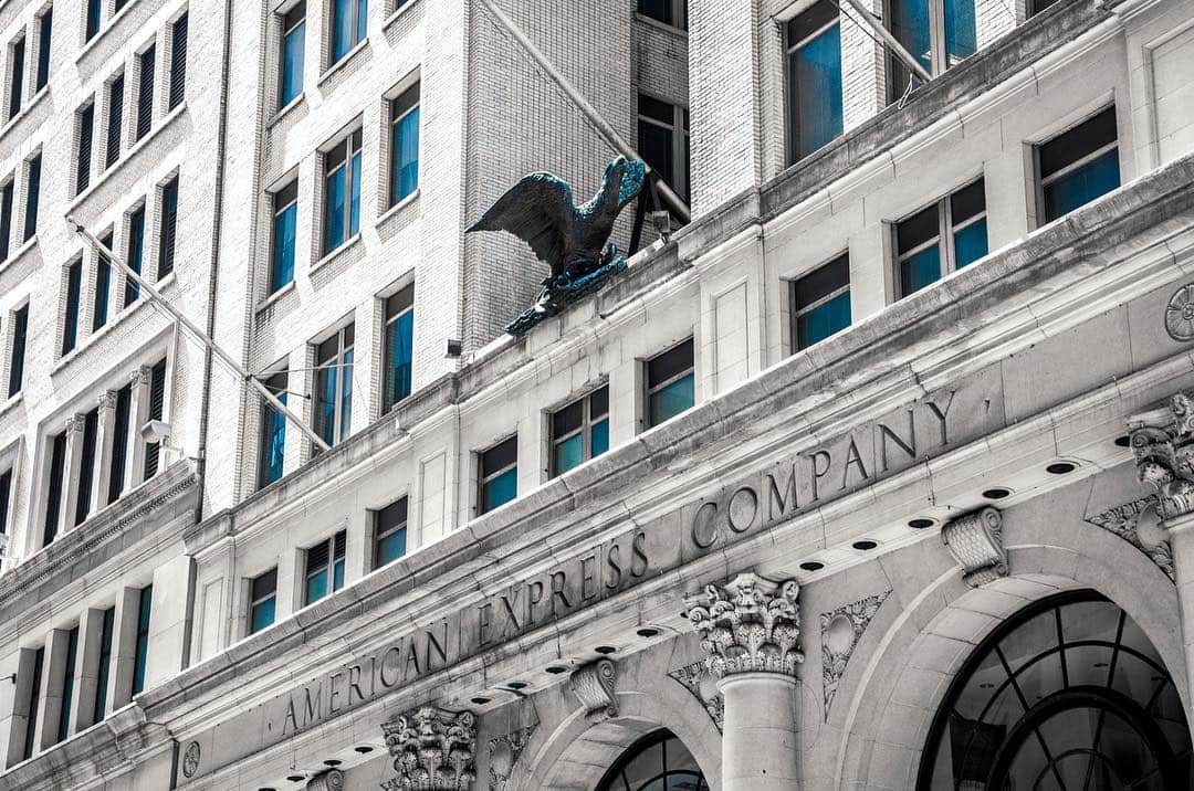Fachada de piedra del edificio de American Express, con el rótulo grabado y una escultura sobre la cornisa.