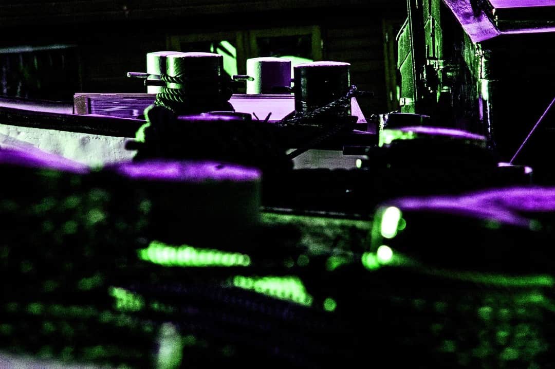 Detalle de un amarre y una embarcación en penumbra, con reflejos verdes y violetas.