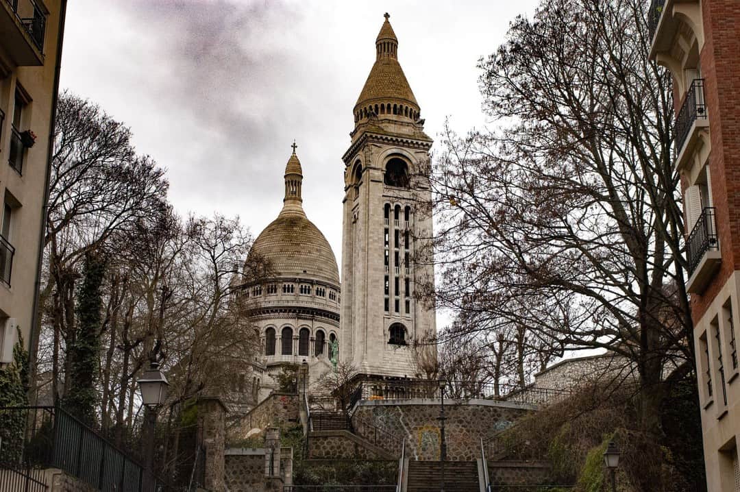 Basílica del Sacré-Cœur al fondo de una calle de Montmartre, entre árboles desnudos.