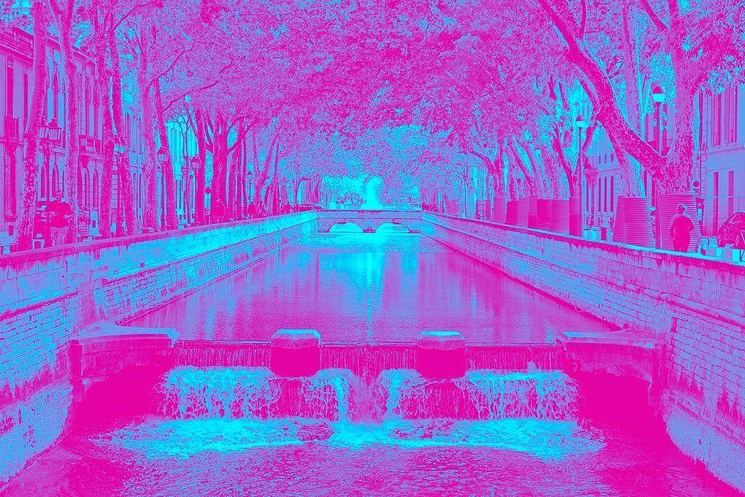 Canal urbano con hileras de árboles, con la imagen virada a rosa y azul turquesa.
