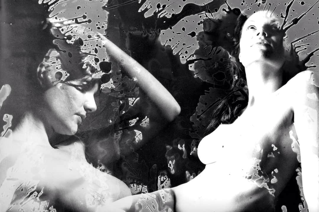 Composición en blanco y negro de alto contraste con dos figuras clásicas femeninas entre manchas.