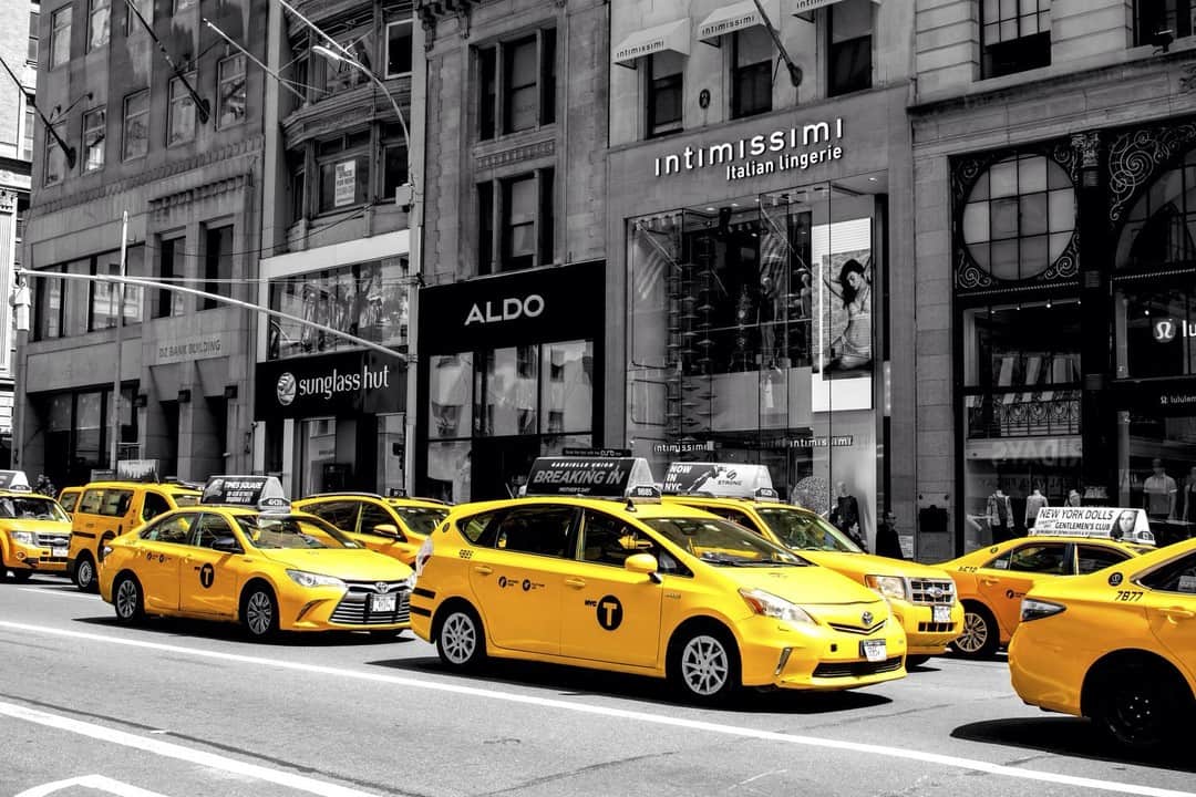 Fila de taxis amarillos parados ante los escaparates de una calle de Nueva York, con el resto en blanco y negro.