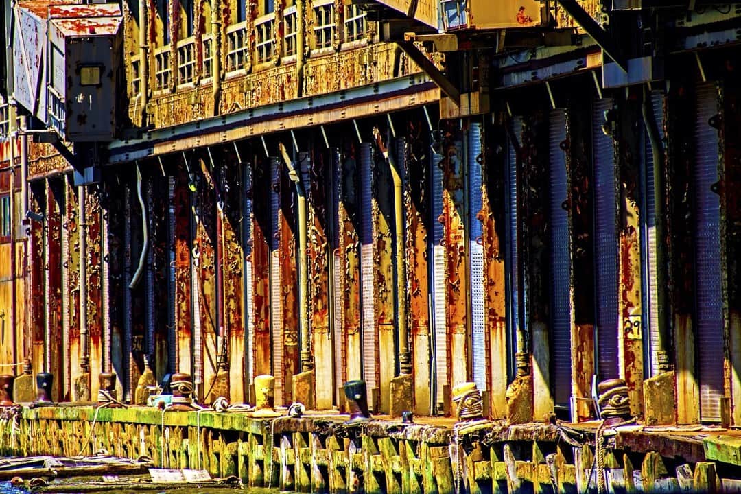 Fachada de una nave antigua con hileras de columnas y vigas de madera, con los colores muy saturados.