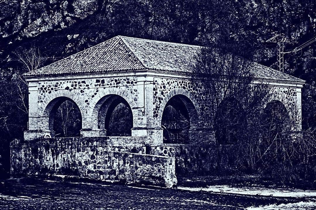 Puente o edificio de piedra con arcos junto al río, con la imagen virada a azul oscuro.